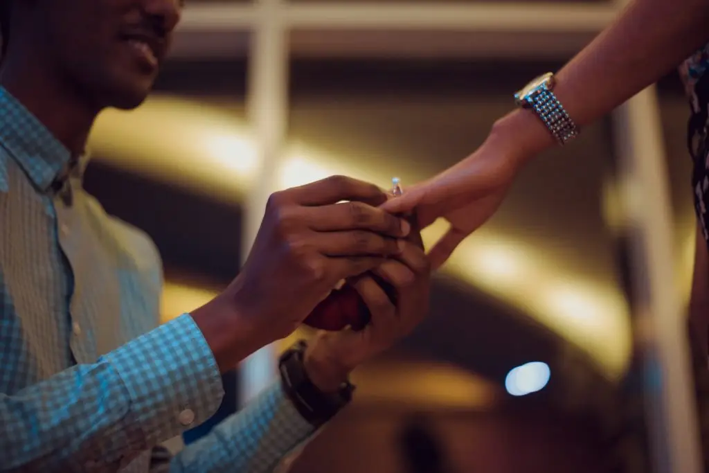 man proposing and putting diamond engagement ring on woman's finger