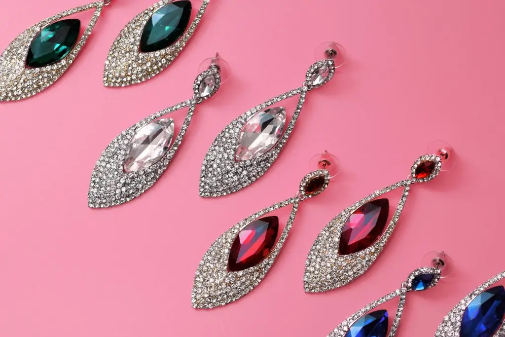 pairs of diamond earrings with colored gemstones on a pink background