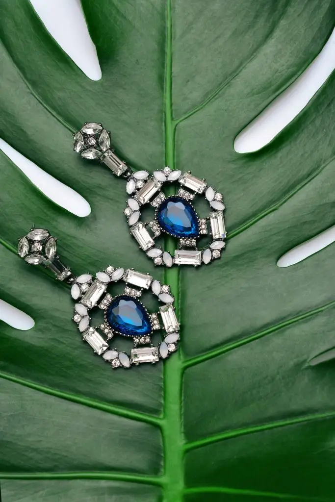 pair of diamond and sapphire earrings on large green leaf