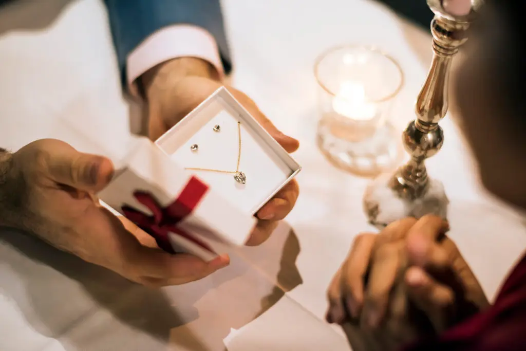 man presenting gift of pendant and earrings to woman at dinner table