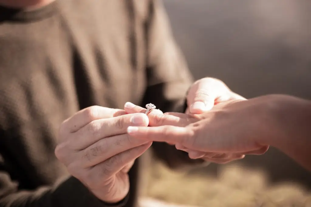 man placing diamond engagement ring on woman's finger after a summer proposal