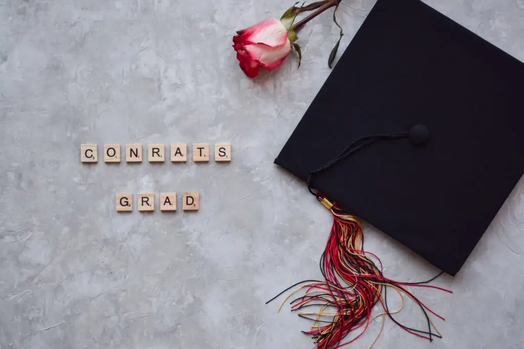 graduation cap, rose, and scrabble tiles that read "congrats grad" on a gray background