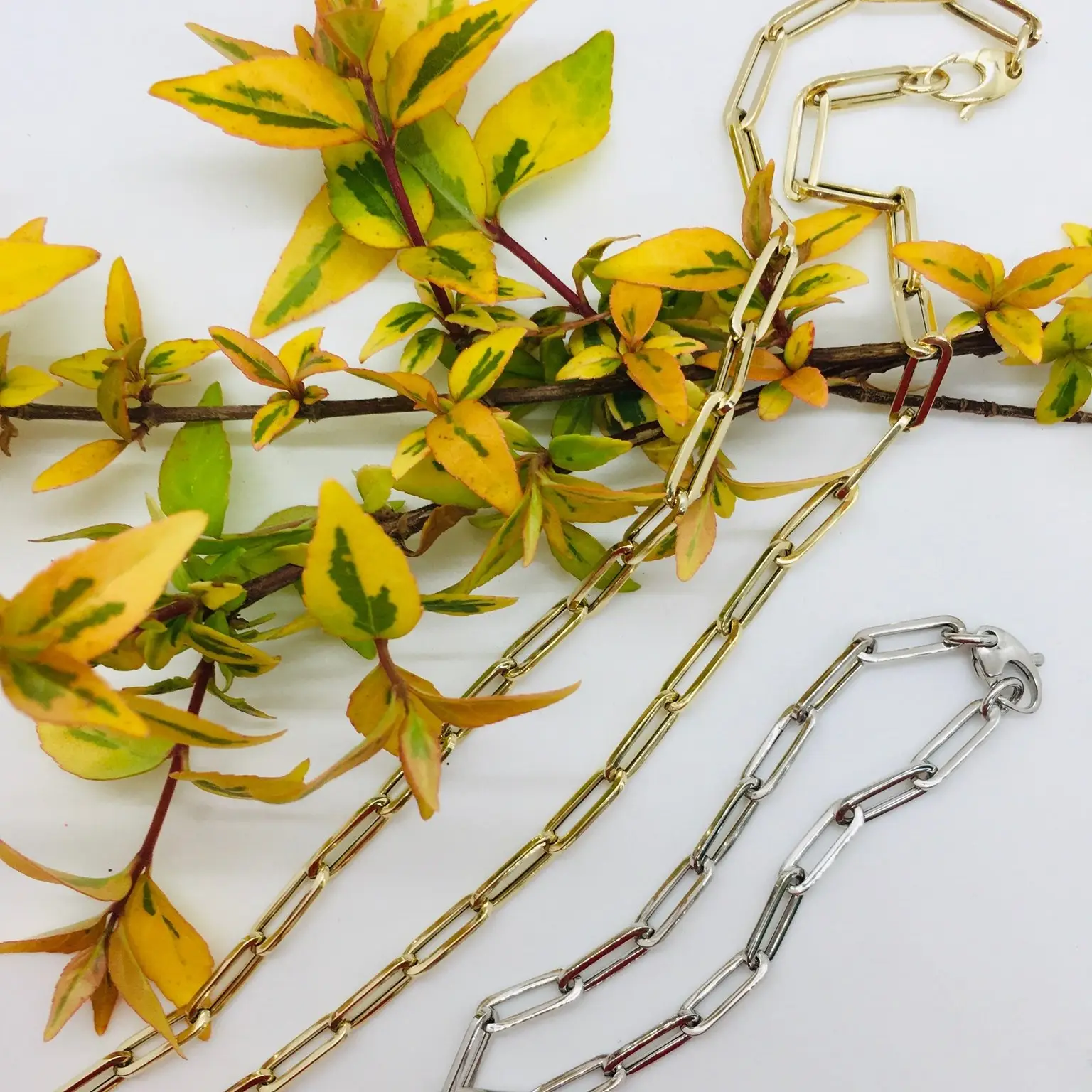 silver and gold paper clip chain necklaces styled next to a yellow and green flower arrangement