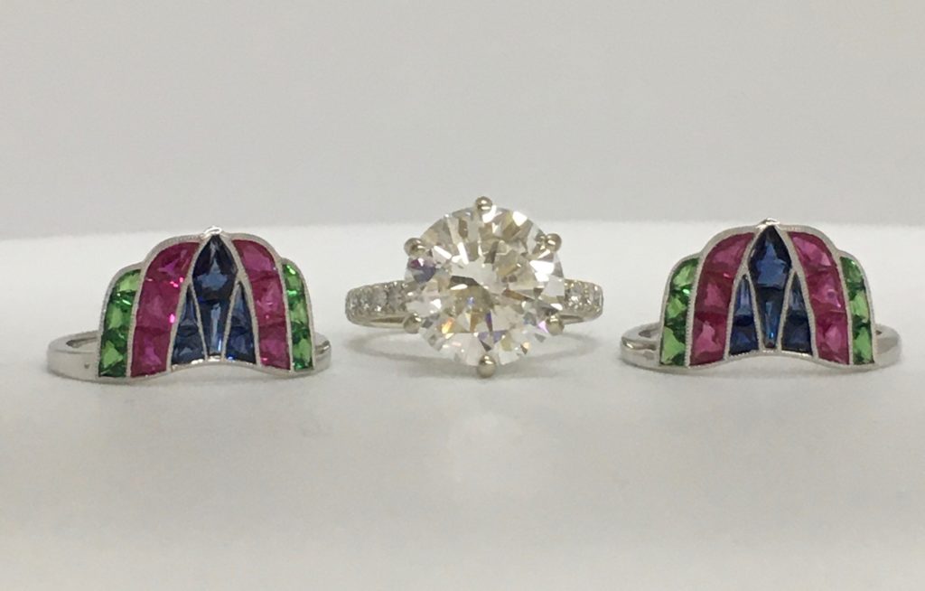 emerald, pink, and dark blue ring wraps displayed on each side of a solitaire diamond ring