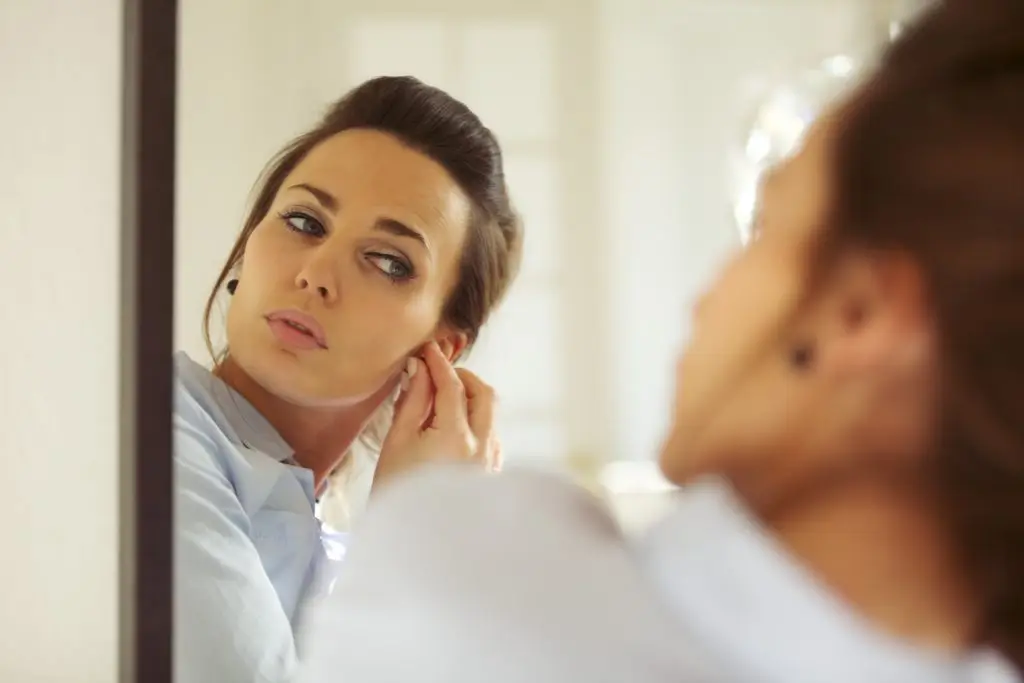 woman looking in a mirror and choosing the right earrings for every face shape