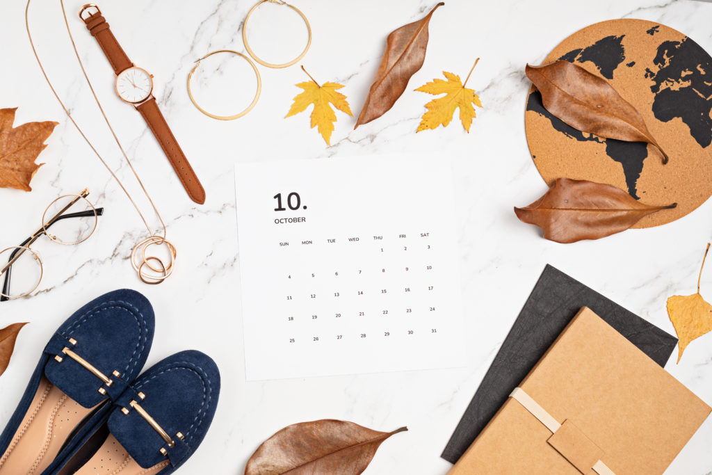 flat lay October calendar surrounded by fall jewelry pairings, shoes, and leaves