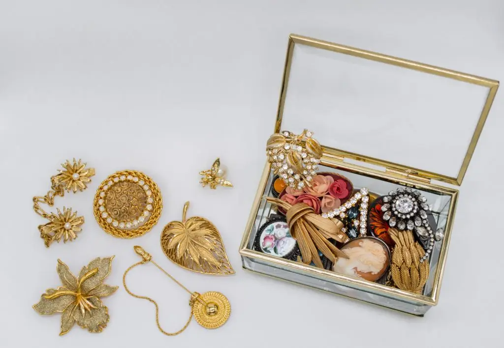 glass jewelry box with gold trim filled with antique jewelry sitting next to antique gold pins