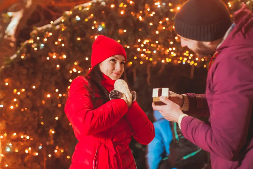 woman being proposed to with an engagement ring next to a Christmas tree on Christmas