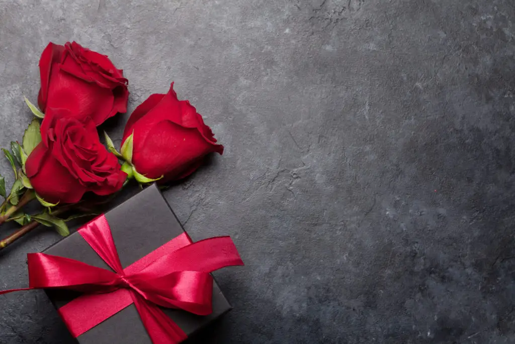 red roses next to a wrapped jewelry gift for Valentine's Day on a rough black background