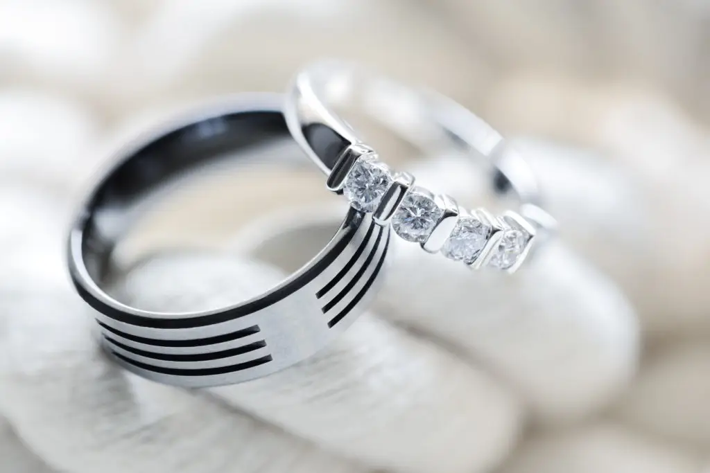 a men's platinum wedding band next to a women's platinum and diamond ring