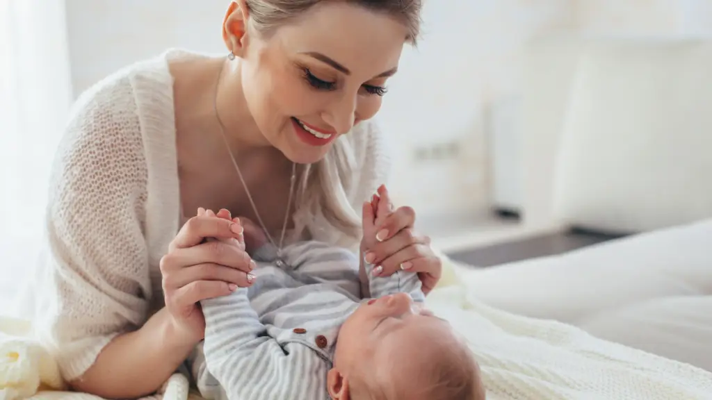 a mother is leaning over her baby holding his hands wearing her new mom jewelry gifted to her