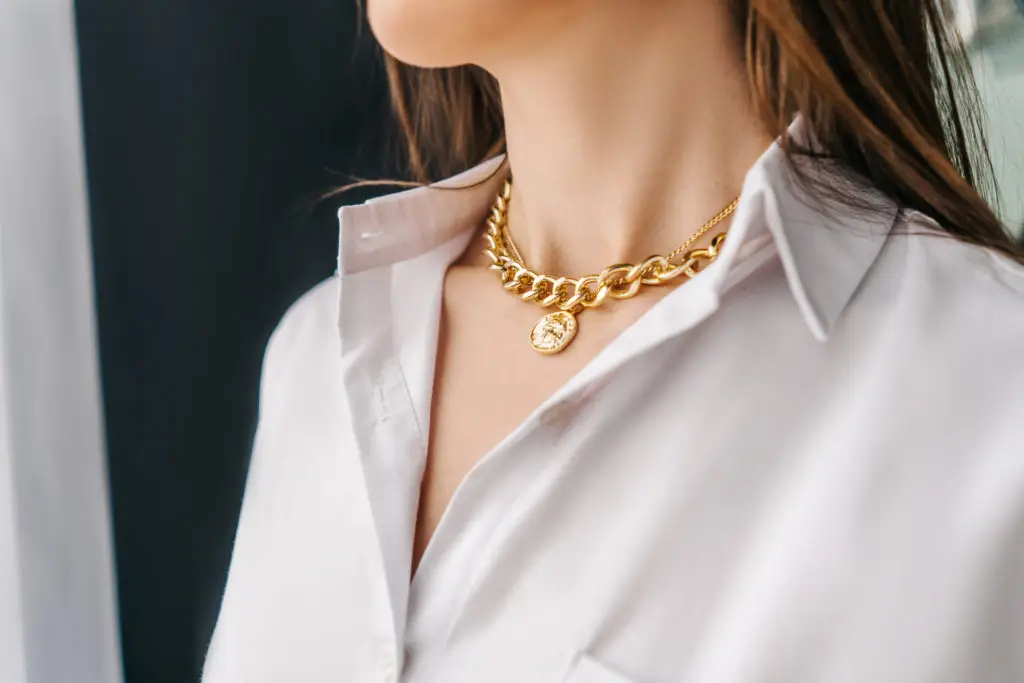 woman wearing gold chain necklace and thin gold pendant necklace with a white button up top as part of the 2022 Fall Jewelry Trends