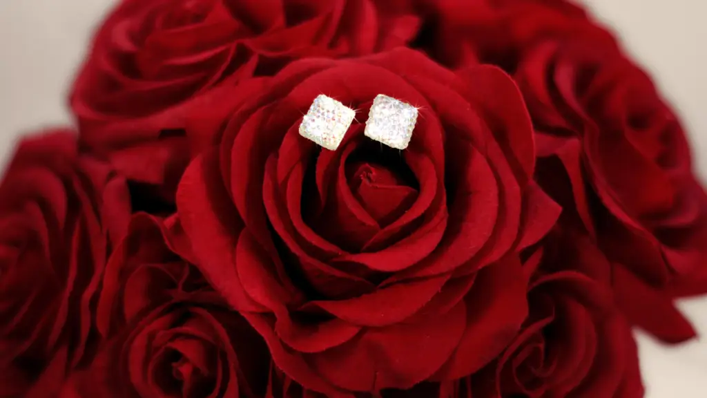 a set of square cut diamond earrings sitting upon a red rose