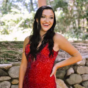 Woman smiling in her red prom dress with hand on her hip. 