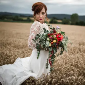 A boho style bride posing in a field with a lacy dress and wild bouquet of flowers