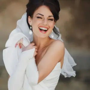 a glamorous bride smiling at the camera wearing large pearl and diamond statement earrings