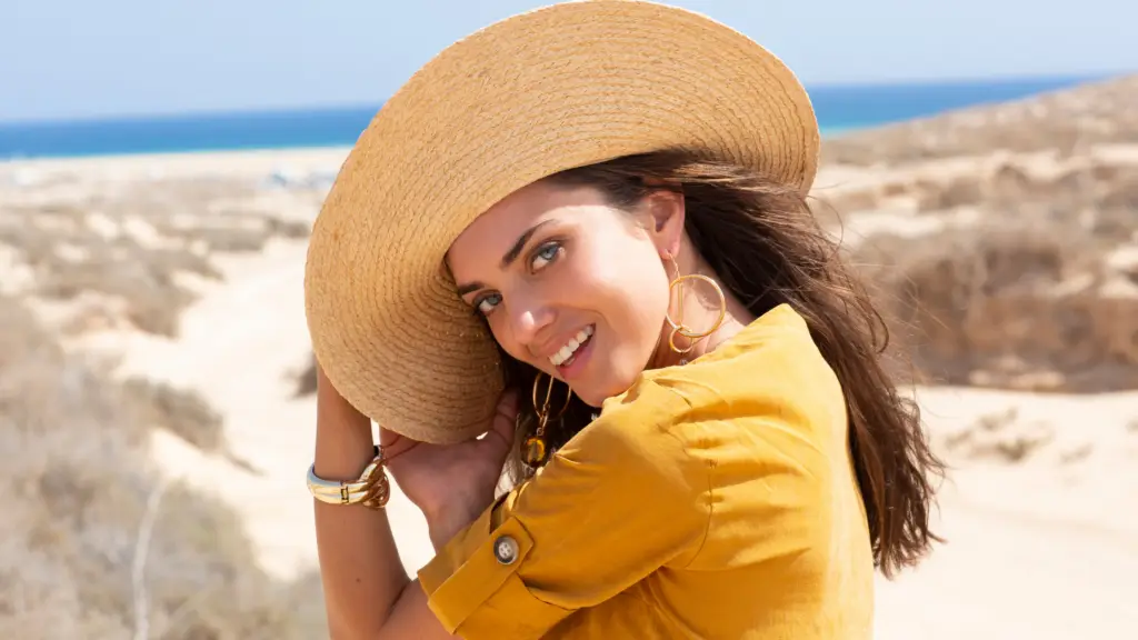 Woman smiling at the beach wearing a wide brimmed hat wearing summer jewelry