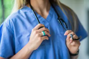 female medical professional wearing blue scrubs and holding a stethoscope around her neck wearing silicone rings with gemstones