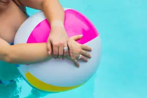 Woman in pool with hands clasped over a colored beach ball wearing her diamond silicone rings