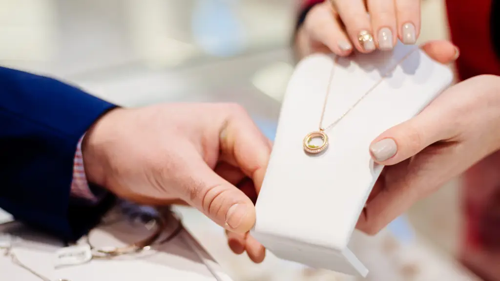 A jeweler showing a gold diamond necklace to a customer and explaining common jewelry terms.