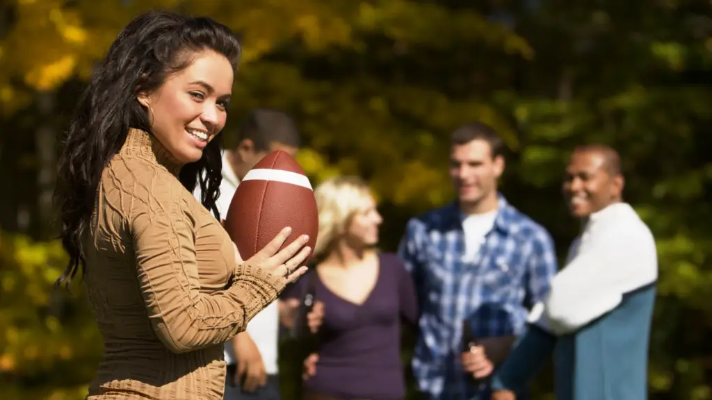 Girl holding football wearing her game day jewelry while friends are smiling in the background