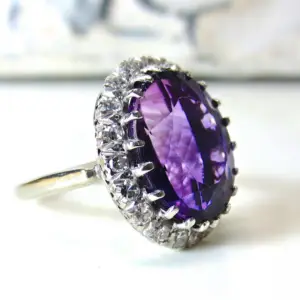 A large amethyst gemstone ring surrounded by tiny white diamonds on a white background