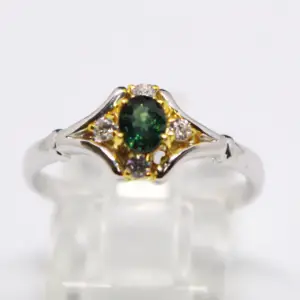 A ring with an oval emerald gemstone surrounded by white diamonds in a yellow gold setting