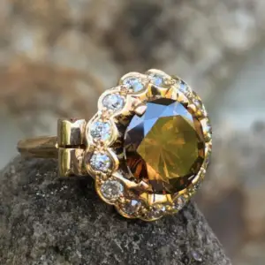 An orange brown diamond ring with white diamonds surrounding it in yellow gold