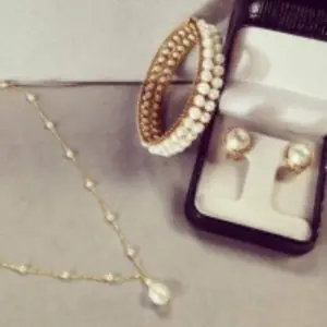 a pearl necklace, pearl bracelet and pearl stud earrings on a neutral background