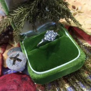 A diamond ring in a green velvet box under an evergreen branch