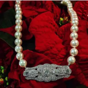 A pearl necklace with an antique diamond brooch set on a background red poinsettia flowers