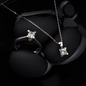 A diamond ring and diamond solitaire necklace set in silver on a black background