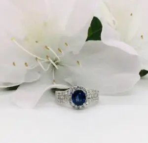 A large oval blue sapphire ring with diamond next to a white flower