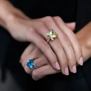 woman's hands wearing a yellow gemstone ring and a blue gemstone ring