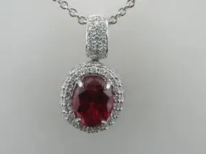 An oval ruby center stone surrounded by diamonds in a pendant necklace