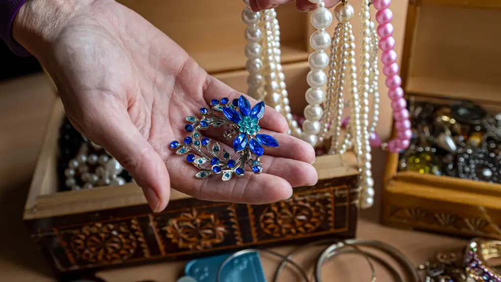 woman holding a blue floral inspired brooch with a jewelry box behind it